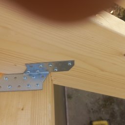 Timber House Tomasz Wojciechowski - Połączenie drewnianych elementów konstrukcyjnych domu za pomocą metalowej płytki i śrub, widok z bliska na detale łączenia.