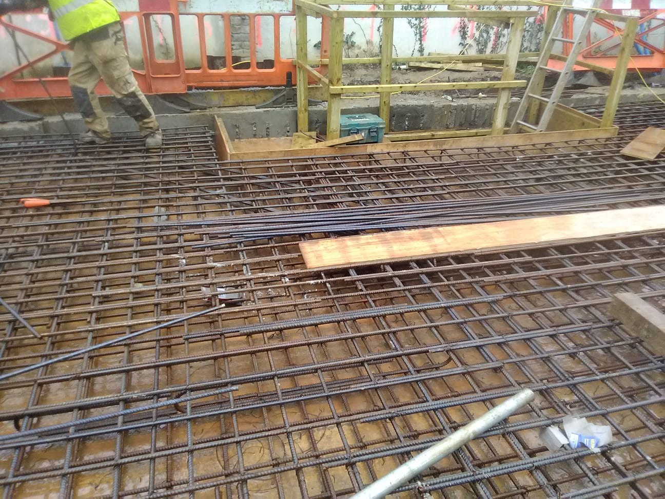 Zbrojenie fundamentu domu z widoczną siatką stalową, deskowaniem i robotnikiem w odblaskowej kamizelce. Detal z placu budowy w trakcie prac.