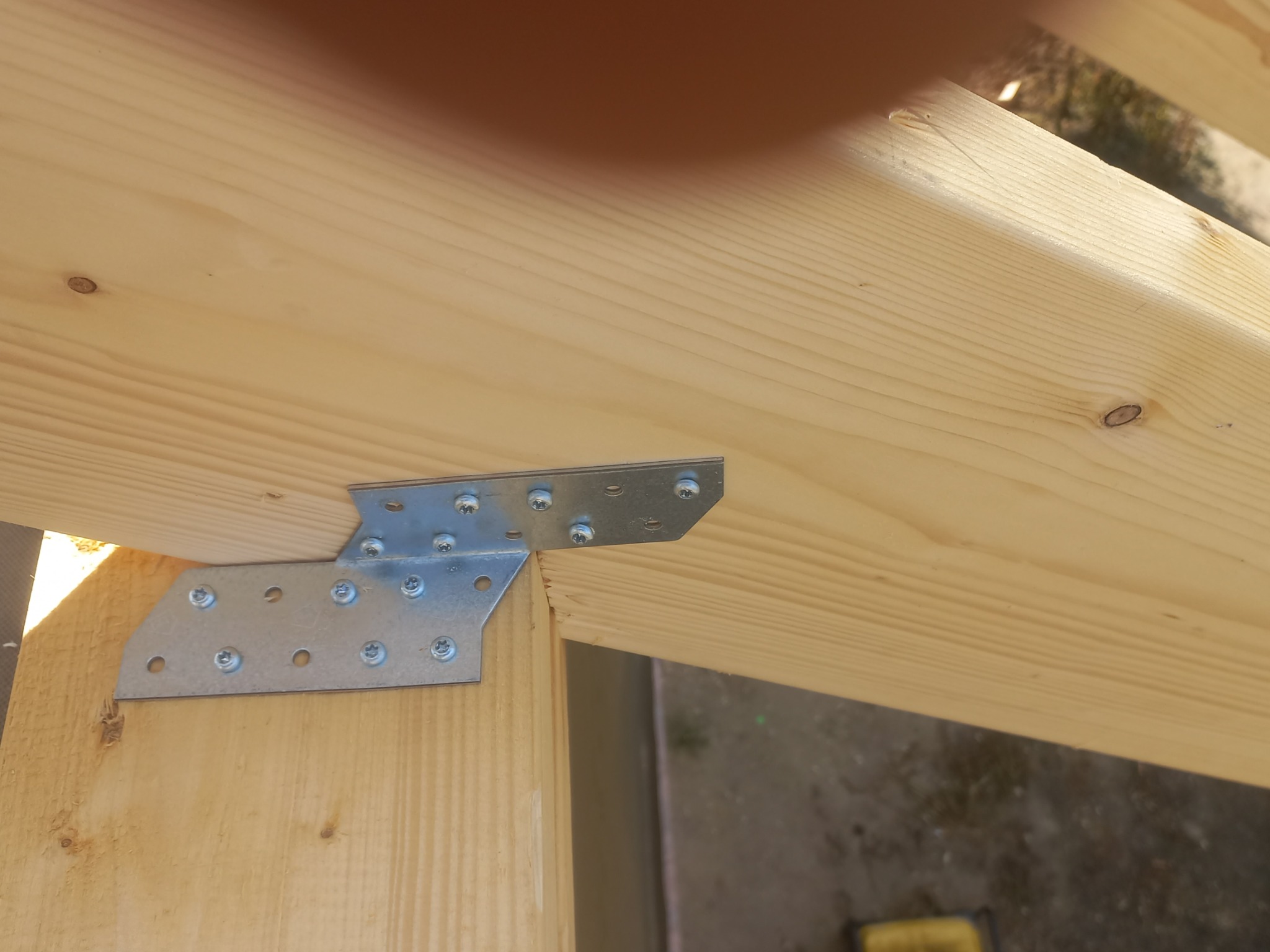 Połączenie drewnianych elementów konstrukcyjnych domu za pomocą metalowej płytki i śrub, widok z bliska na detale łączenia.