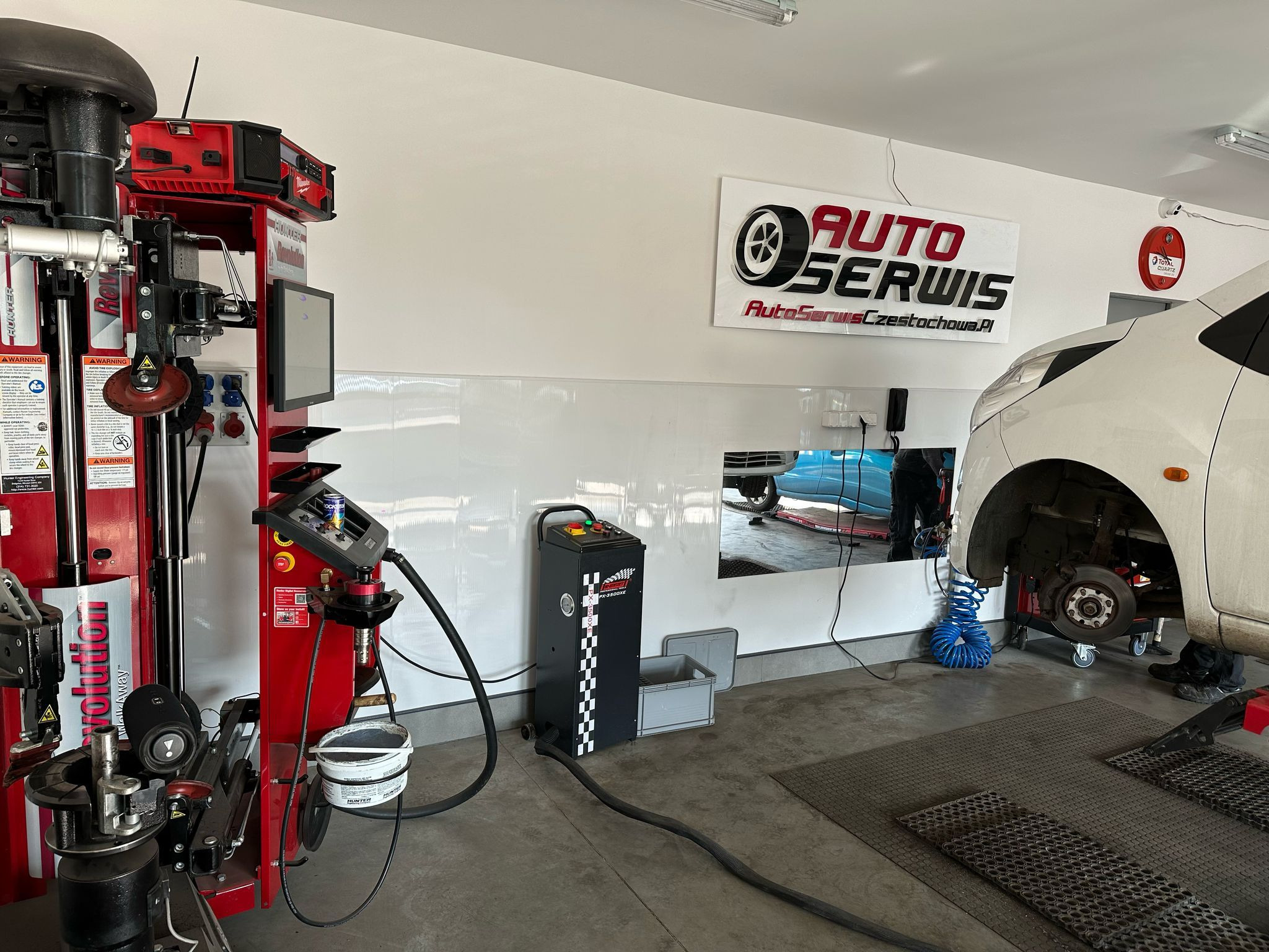 Wnętrze warsztatu: podnośnik z autem bez koła, urządzenia Hunter do geometrii kół, logo Auto Serwis Częstochowa na ścianie, narzędzia i wyposażenie.