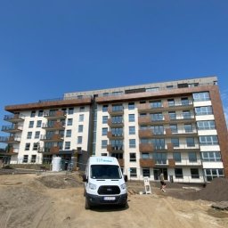 Win Bud - Nowoczesny budynek wielorodzinny w Gdyni Hossa, z balkonami i oknami, na placu budowy z dwoma samochodami dostawczymi firmy Widok.