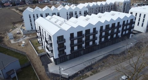 Nowoczesne budynki wielorodzinne z balkonami w Redzie. Charakterystyczna, biała elewacja i czarne ramy okienne. Ujęcie z drona ukazuje geometrię dachów.