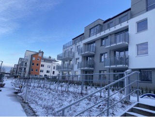 Nowoczesny budynek wielorodzinny z balkonami o szklanych balustradach w zimowej scenerii, Gdynia Hossa, z niską perspektywą podkreślającą architekturę.