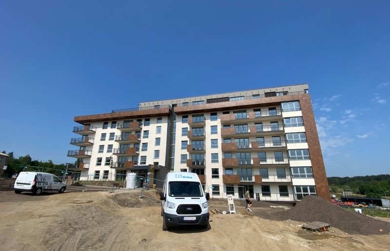 Nowoczesny budynek wielorodzinny w Gdyni Hossa, z balkonami i oknami, na placu budowy z dwoma samochodami dostawczymi firmy Widok.