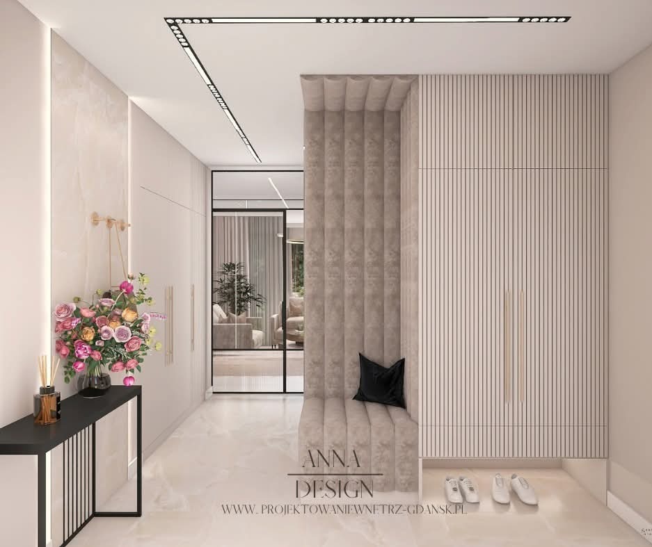 Elegancki przedpokój w jasnych barwach z siedziskiem obitym tkaniną, minimalistyczną konsolą z kwiatami i szafą z pionowymi frezami. Subtelne oświetlenie punktowe.