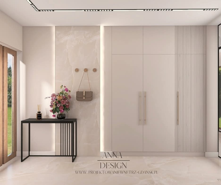 Jasny przedpokój z szafą w zabudowie, konsolą i kwiatami. Na ścianie wieszaki z torebką. Uwagę zwraca podświetlenie LED pionowych paneli ściennych.
