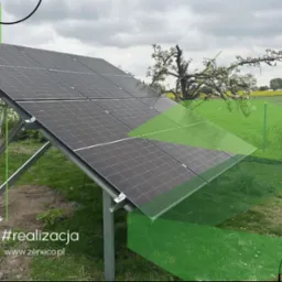 Instalacja paneli słonecznych na łące, widok z dołu. Metalowa konstrukcja wspiera panele, w tle drzewa i pole. Graficzne elementy w odcieniach zieleni.
