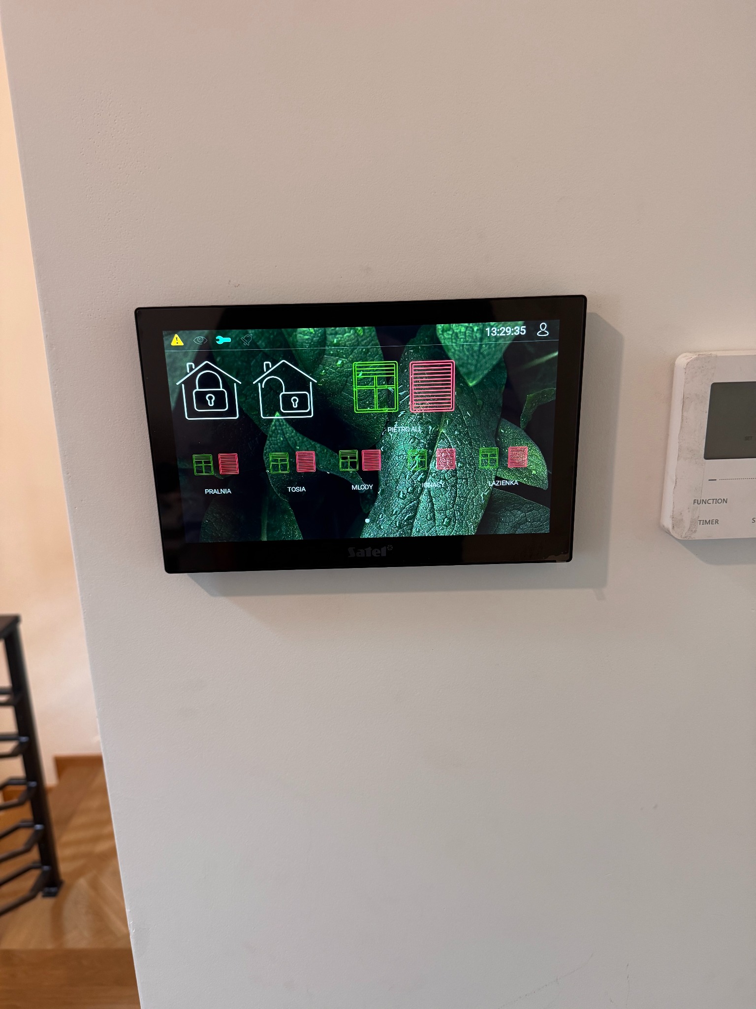 Panel sterowania systemem alarmowym Satel, zamontowany na ścianie w Mińsku Mazowieckim. Widoczne ikony i nazwy pomieszczeń: pralnia, Tosia, młody, piętro all, Ignacy, łazienka.