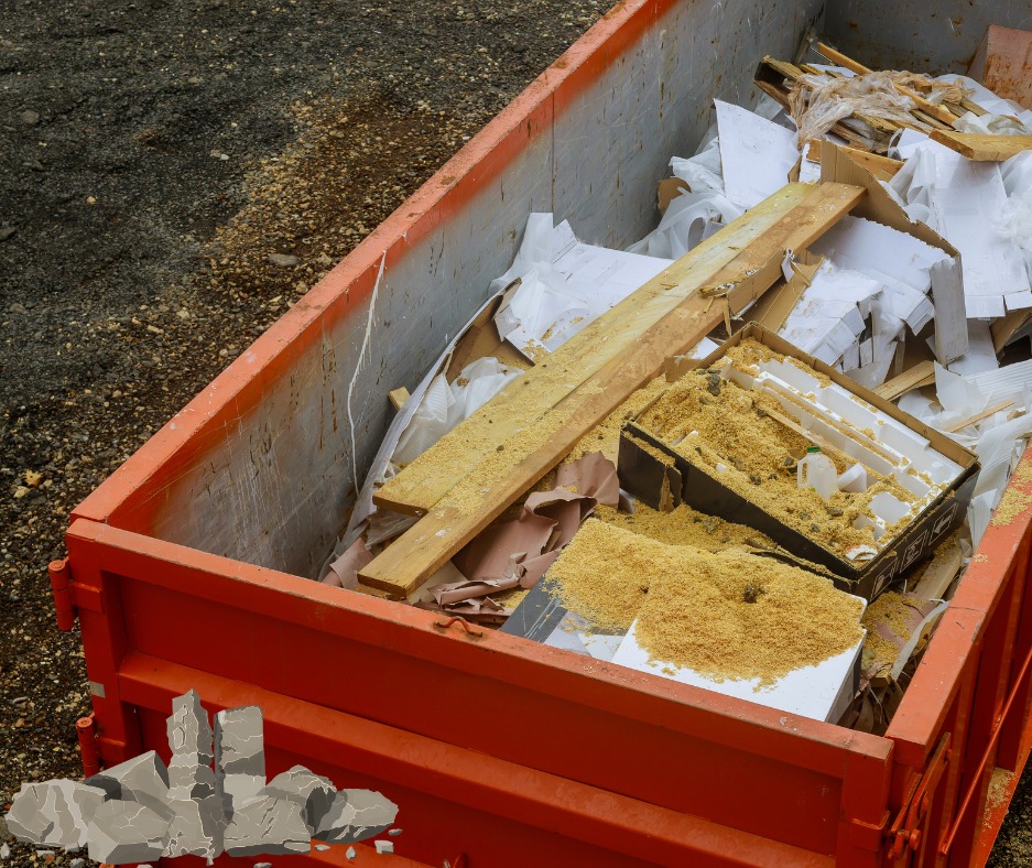 Pomarańczowy kontener wypełniony gruzem, drewnem i odpadami budowlanymi. Widok z góry, z ziemią w tle.