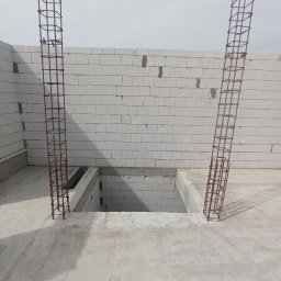 Matiitsiv - Dwie pionowe konstrukcje zbrojeniowe wystające z betonowej wylewki, ściany z białych bloczków, otwór w podłodze. Etap prac budowlanych.
