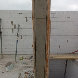 Matiitsiv - Wznoszenie żelbetowego słupa w szalunku drewnianym z widocznym zbrojeniem. Ściany z bloczków betonu komórkowego w tle. Element konstrukcyjny w trakcie budowy.