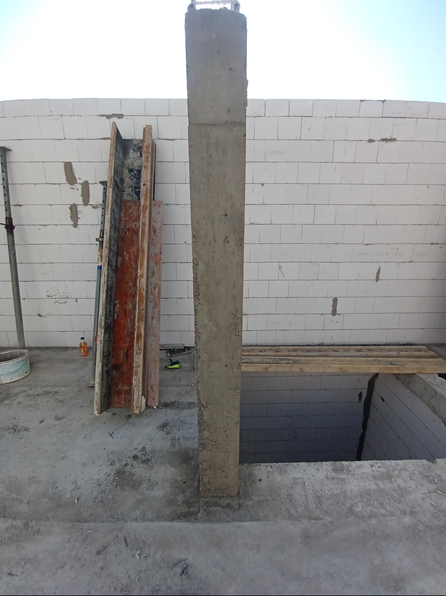 Betonowy słup w trakcie budowy domu we Wrocławiu. Widoczne szalunki, ściany z bloczków i otwór w fundamencie. Prace budowlane w toku.