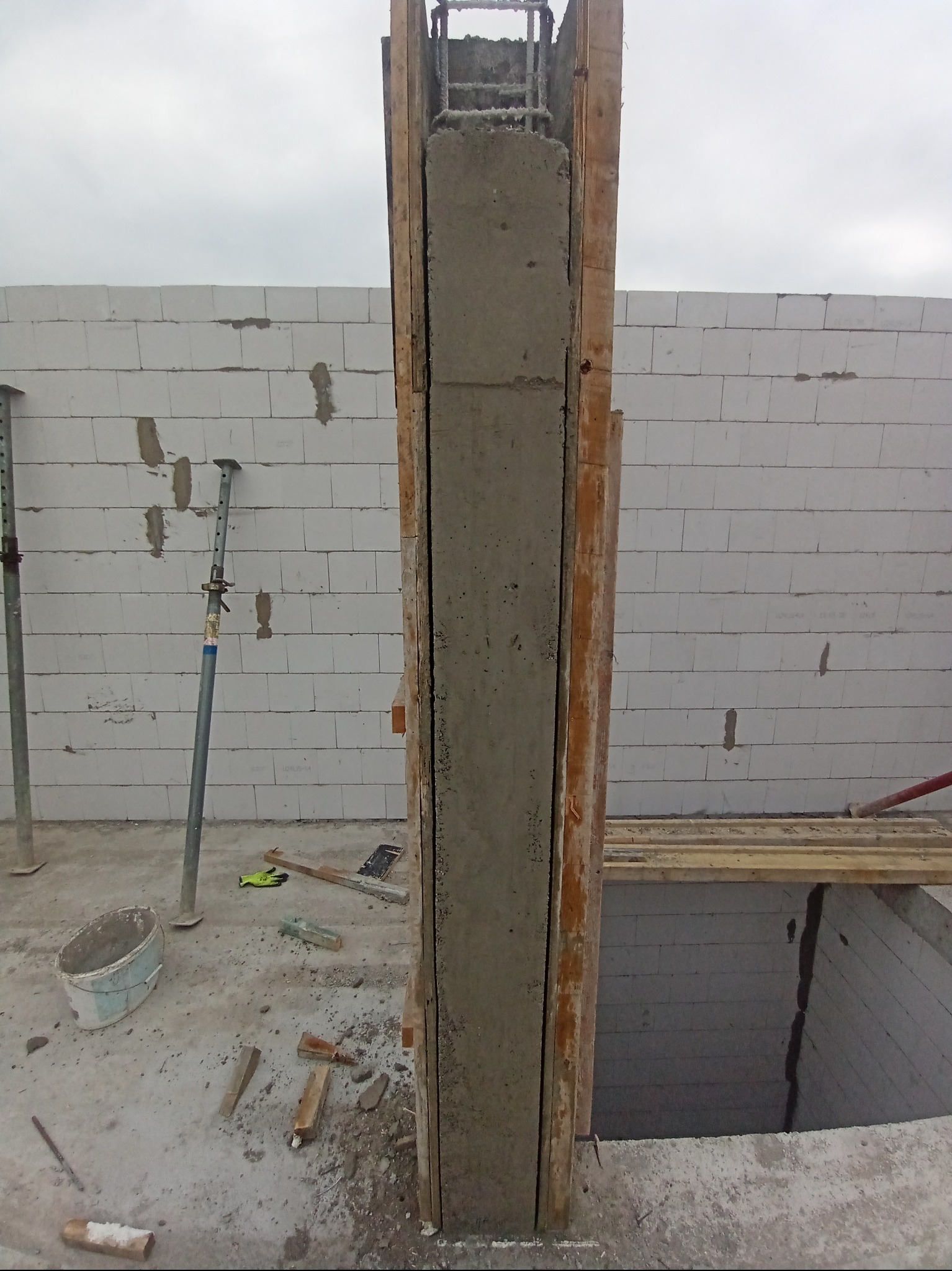 Wznoszenie żelbetowego słupa w szalunku drewnianym z widocznym zbrojeniem. Ściany z bloczków betonu komórkowego w tle. Element konstrukcyjny w trakcie budowy.