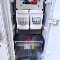 Instal-Max - Otwarta skrzynka elektryczna z bezpiecznikami i przewodami w różnych kolorach. Widoczne elementy instalacji elektrycznej. Detal.