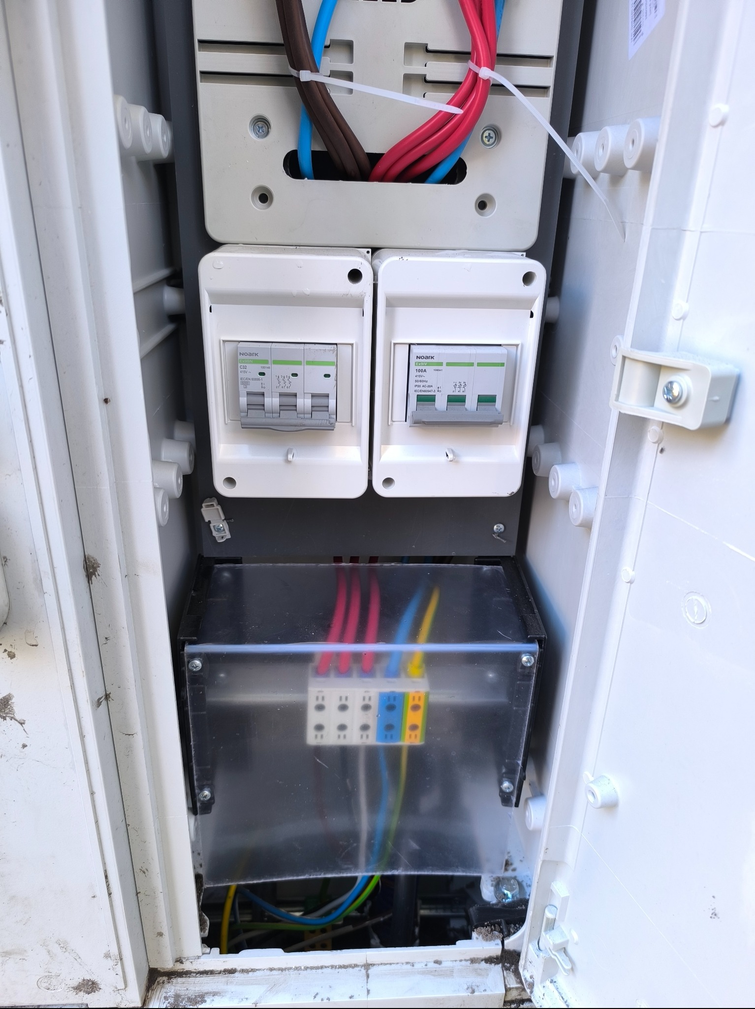 Otwarta skrzynka elektryczna z bezpiecznikami i przewodami w różnych kolorach. Widoczne elementy instalacji elektrycznej. Detal.