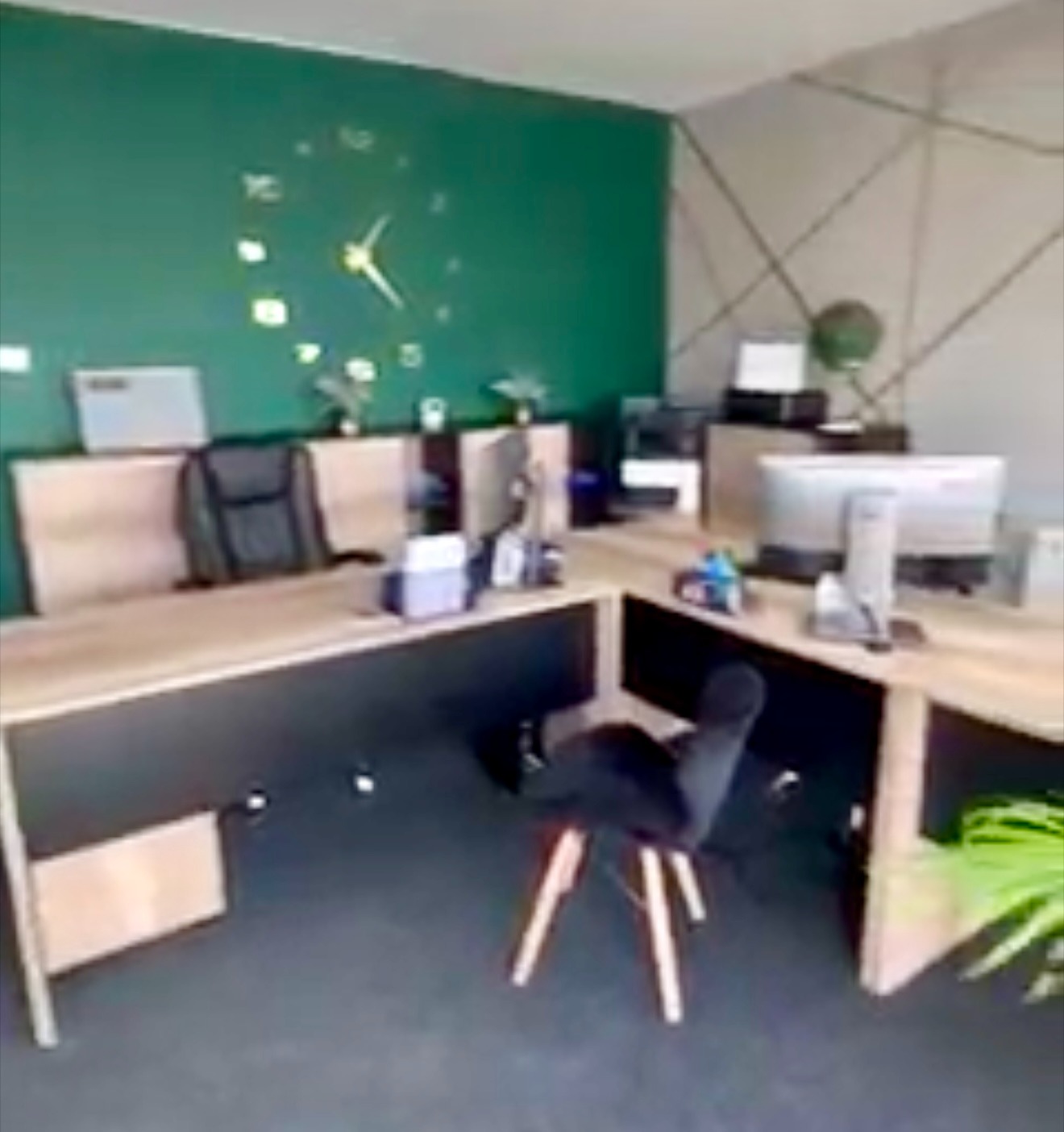 Nowoczesne biuro: zielona ściana z zegarem, drewniane biurka z czarnymi frontami, ergonomiczne krzesła. Profesjonalne i uporządkowane miejsce pracy.