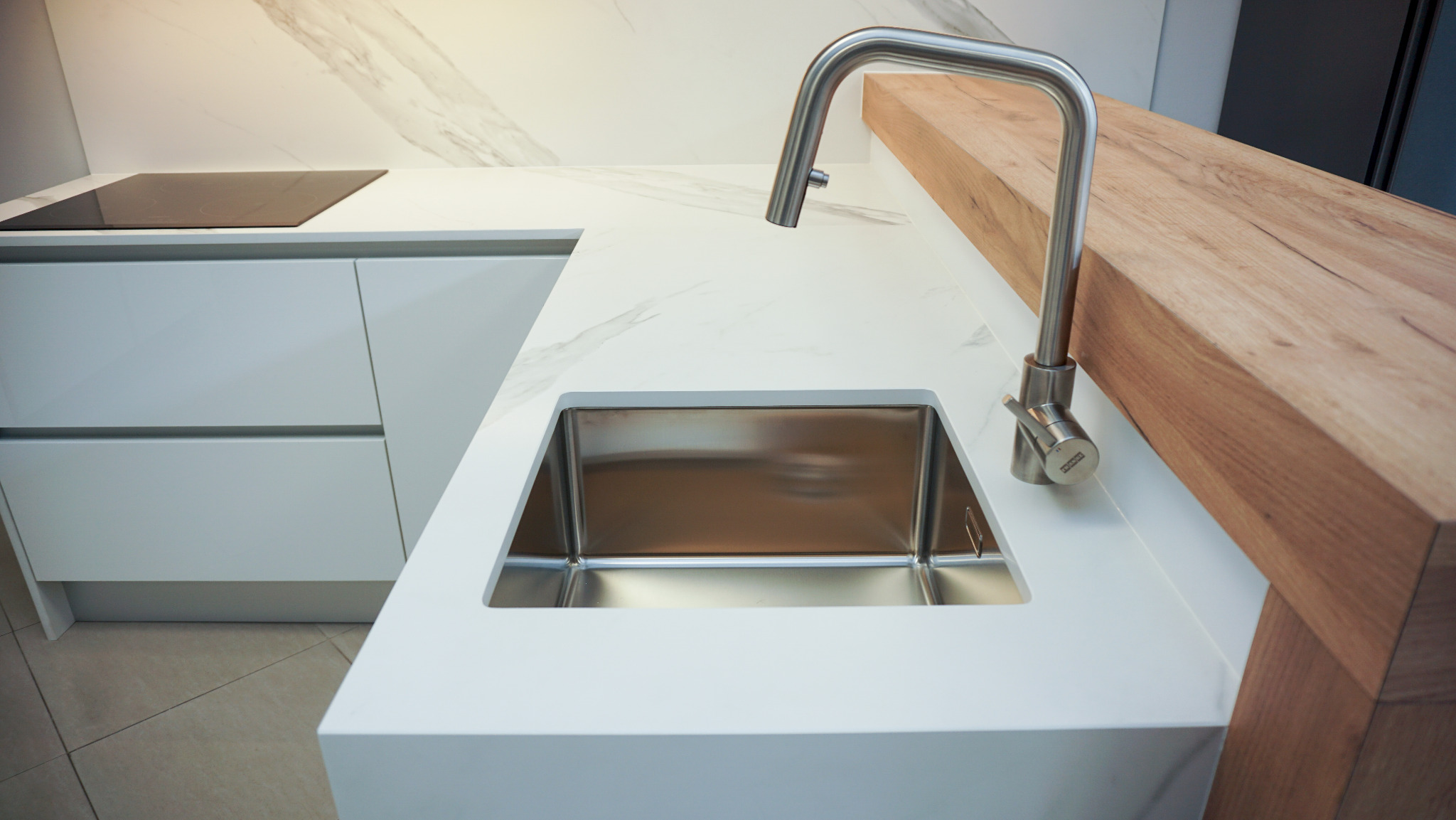 Nowoczesna kuchnia: biały blat z marmurowym wzorem, stalowy zlew i bateria Franke, drewniany panel boczny. Minimalistyczny design, czyste linie.