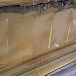 AutoRust Protect - Konserwacja podwozi - Wnętrze progu samochodu po zabezpieczeniu antykorozyjnym; widoczne ślady preparatu, wkręt mocujący i uszczelka. Ujęcie z bliska.