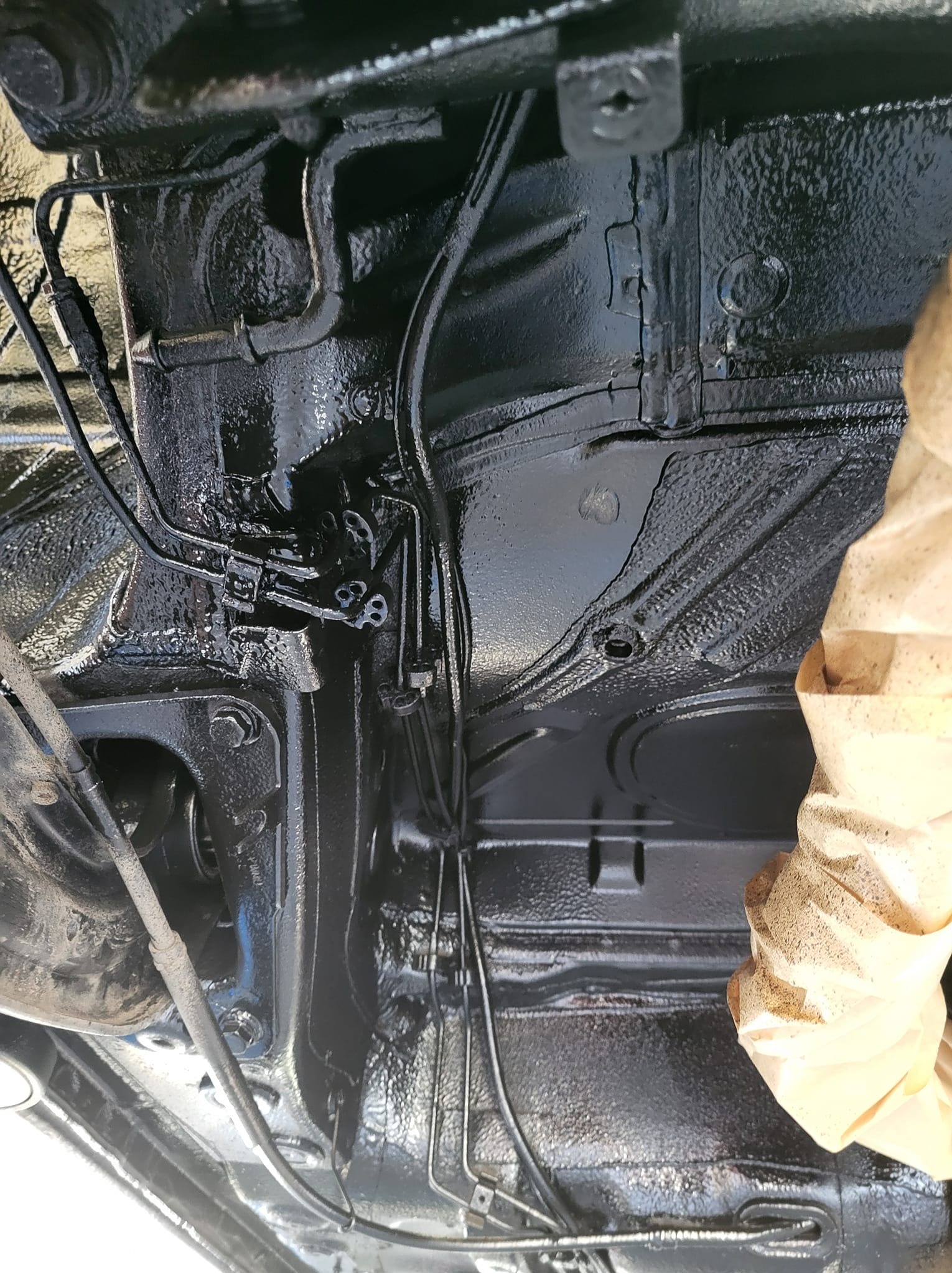 Podwozie samochodu po zabezpieczeniu antykorozyjnym, widoczne elementy zawieszenia i przewody pokryte czarną, błyszczącą powłoką. Fragment maskowania ochronnego.