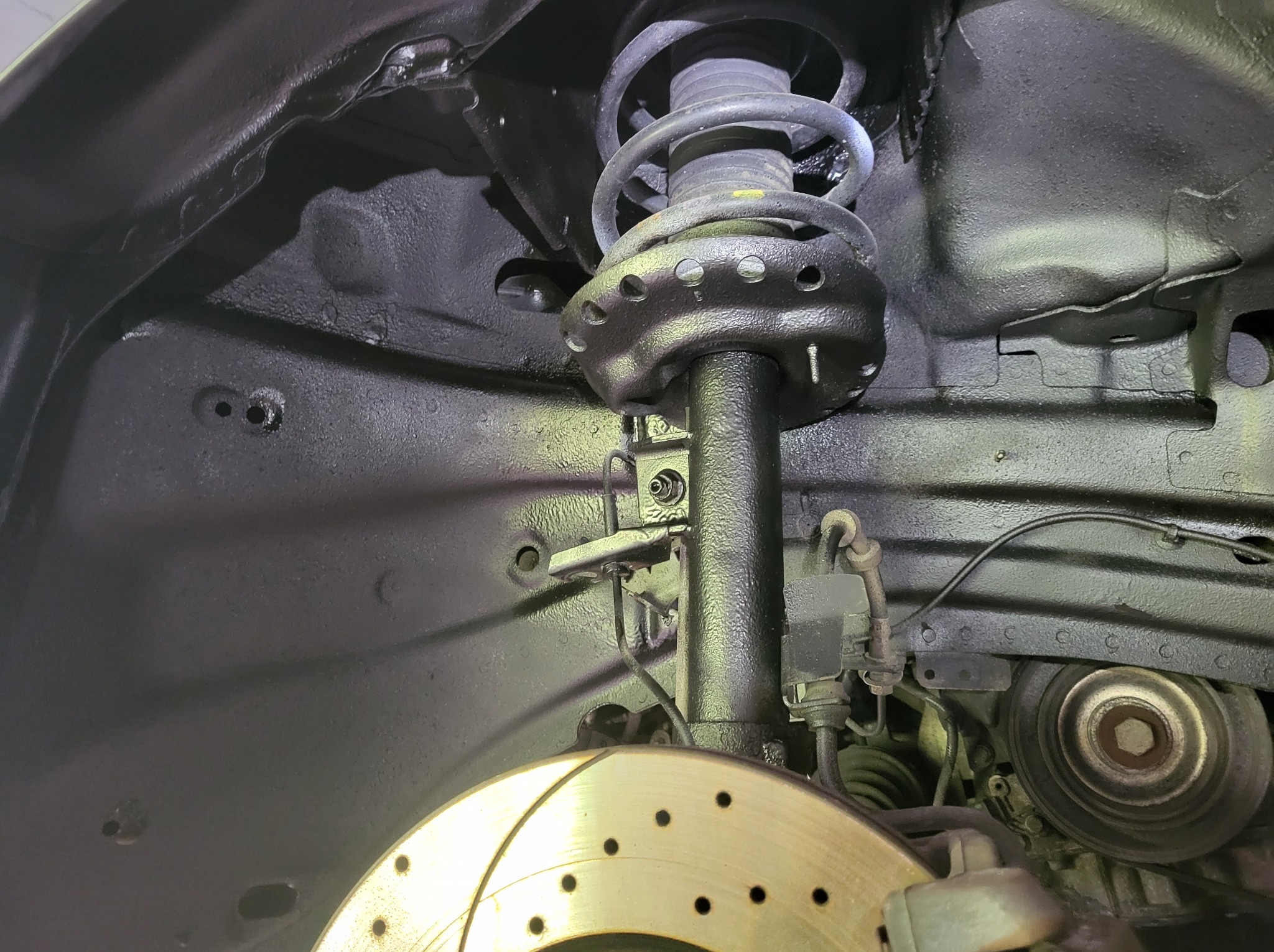 Element zawieszenia samochodu po piaskowaniu i zabezpieczeniu antykorozyjnym, widoczna sprężyna, amortyzator i tarcza hamulcowa.