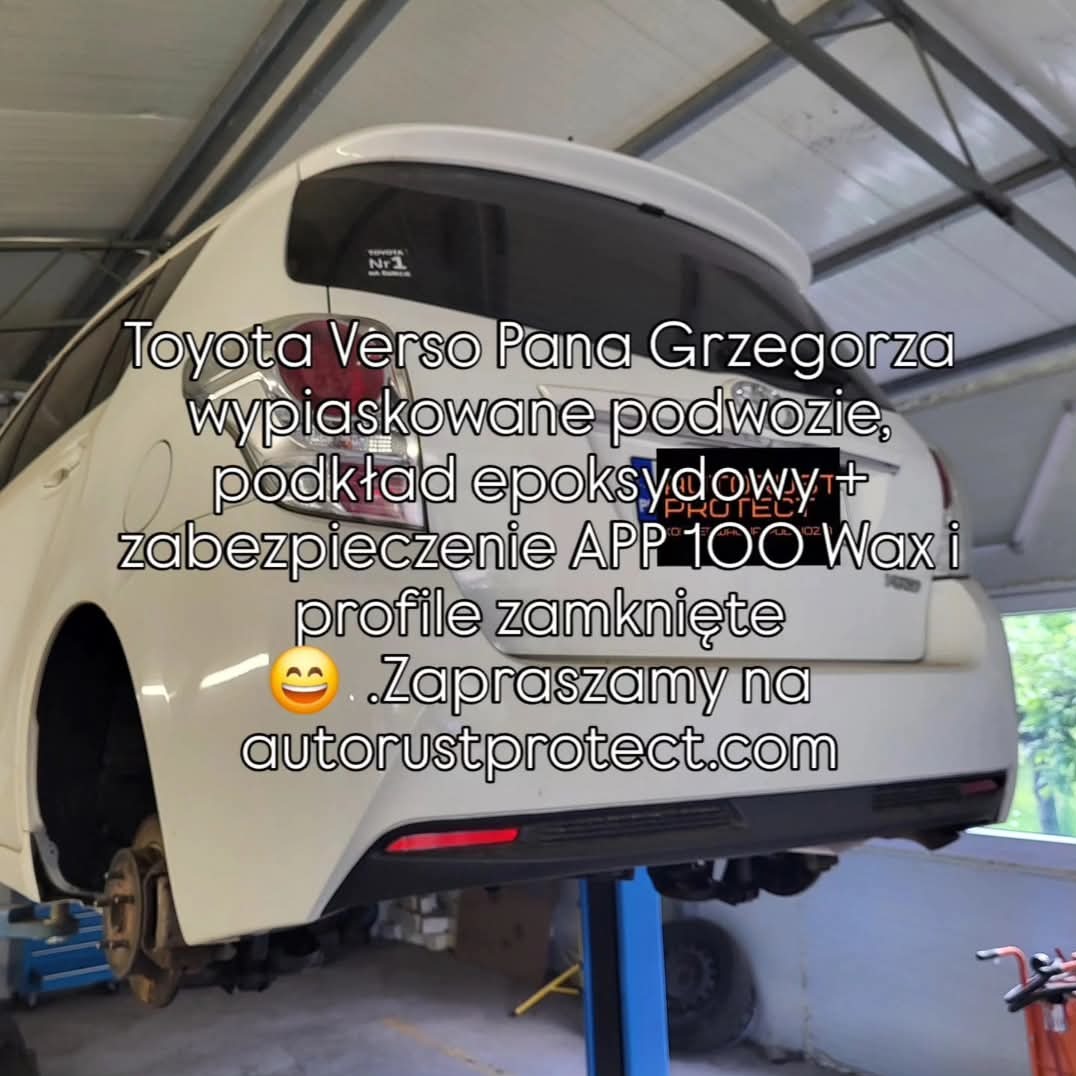 Biała Toyota Verso na podnośniku po piaskowaniu podwozia i zabezpieczeniu antykorozyjnym. Widoczne elementy podwozia bez kół. Reklama firmy autorustprotect.com.