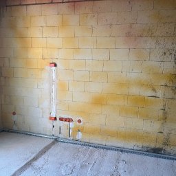 Pro Instal - DAMIAN NOWAK - Wnętrze w trakcie prac elektrycznych: widoczne koryta kablowe przy podłodze i puszki instalacyjne w ścianie z betonu komórkowego. Ściany surowe, z widocznymi śladami po budowie.