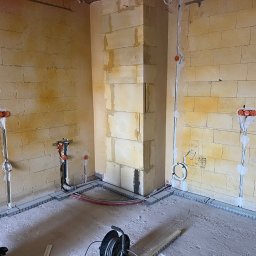 Pro Instal - DAMIAN NOWAK - Wnętrze w trakcie prac instalacyjnych: widoczne kable w peszlach, puszki elektryczne, listwy przypodłogowe. Ściany z bloczków, surowa podłoga. Etap przed tynkowaniem.