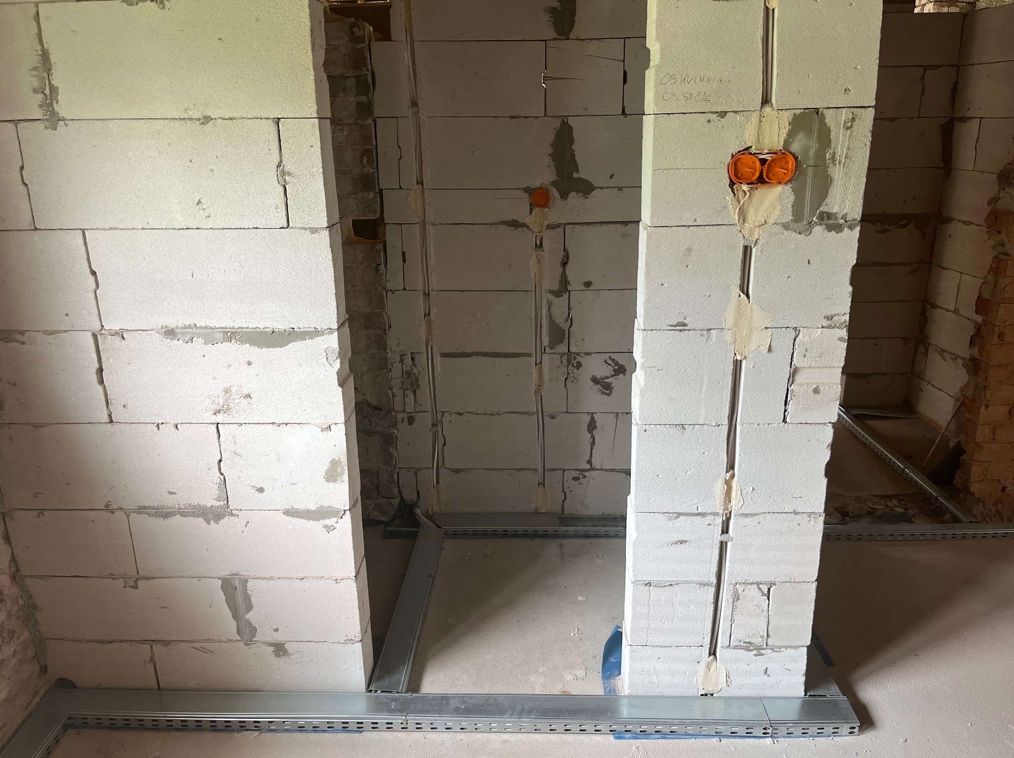 Wykute bruzdy w ścianie z betonu komórkowego pod instalację elektryczną, widoczne puszki elektryczne i koryto kablowe przy podłodze. Prace w trakcie realizacji.