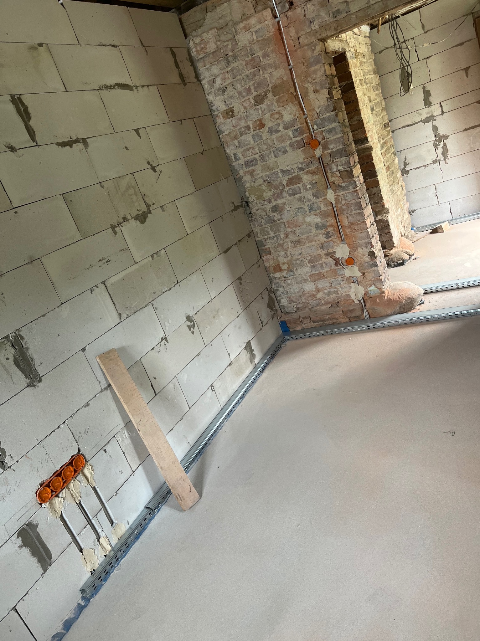 Wnętrze w trakcie prac instalacyjnych: ściany z betonu komórkowego, instalacja elektryczna w peszlach, metalowe profile pod wylewkę, fragment ściany z cegły.