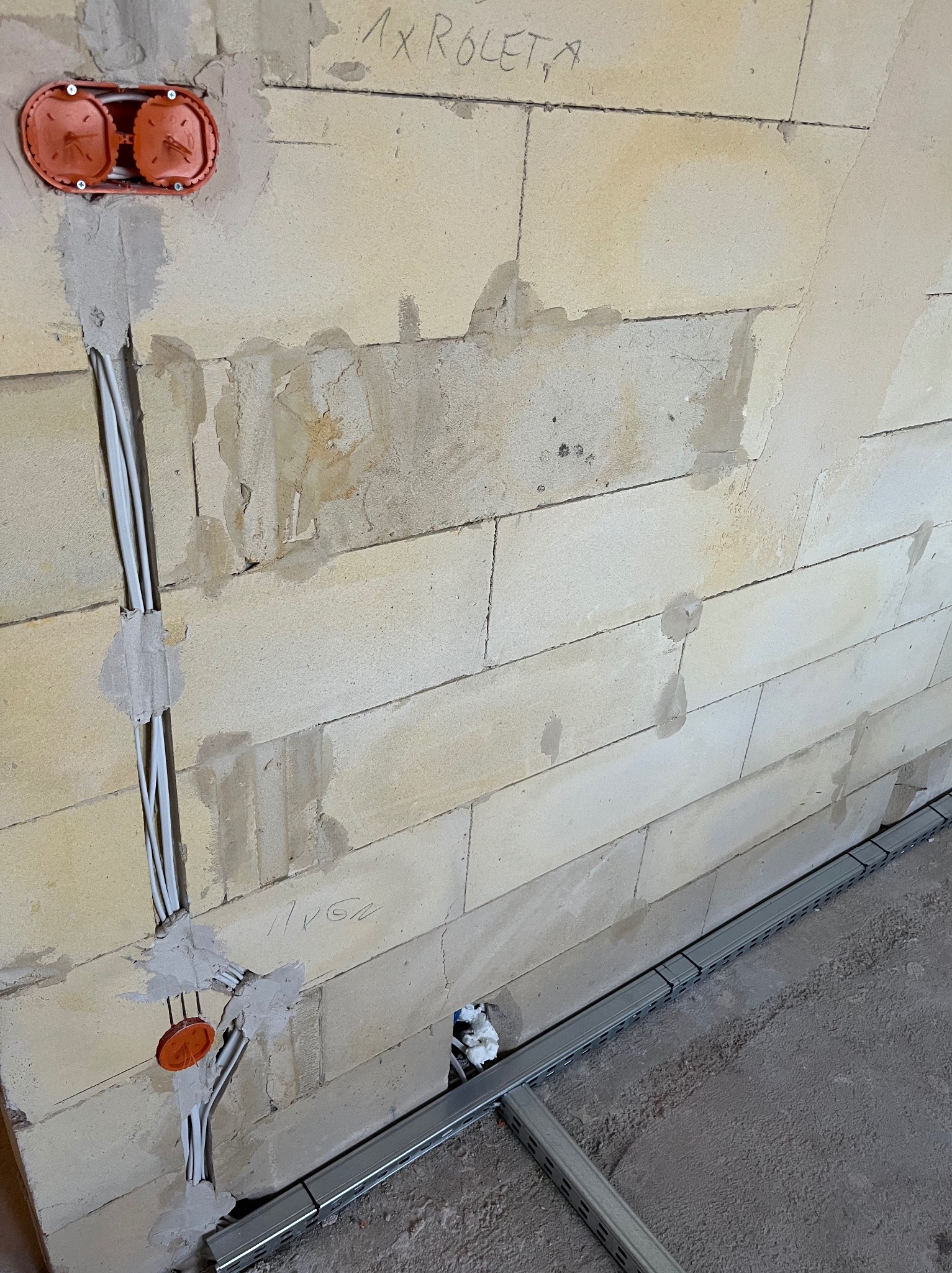 Ściana z betonu komórkowego z zamontowanymi puszkami elektrycznymi i przewodami w bruzdach, przygotowana do dalszych prac wykończeniowych.