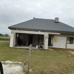 Usługi ogólnobudowlane MasterMaxBud - Surowy dom jednorodzinny w trakcie budowy, z widoczną konstrukcją dachu pokrytą papą, niezadaszony garaż, ściany z bloczków i numer domu na ścianie.