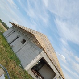 Usługi ogólnobudowlane MasterMaxBud - Budowa domu z betonu komórkowego w trakcie realizacji, widok z dołu na ściany i konstrukcję dachu na tle błękitnego nieba z chmurami.