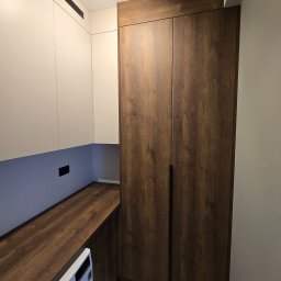 NomadMeble Adam Tatar - Nowoczesna zabudowa: szafa z ciemnego drewna i białe szafki wiszące z wentylacją, uzupełnione blatem z tego samego drewna. Pralka częściowo widoczna.