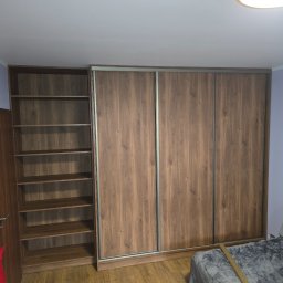 NomadMeble Adam Tatar - Szafa wnękowa z przesuwnymi drzwiami i regałem w odcieniach brązu, wykonana na wymiar w Kleczy Górnej. Widoczna struktura drewna i metalowe prowadnice.