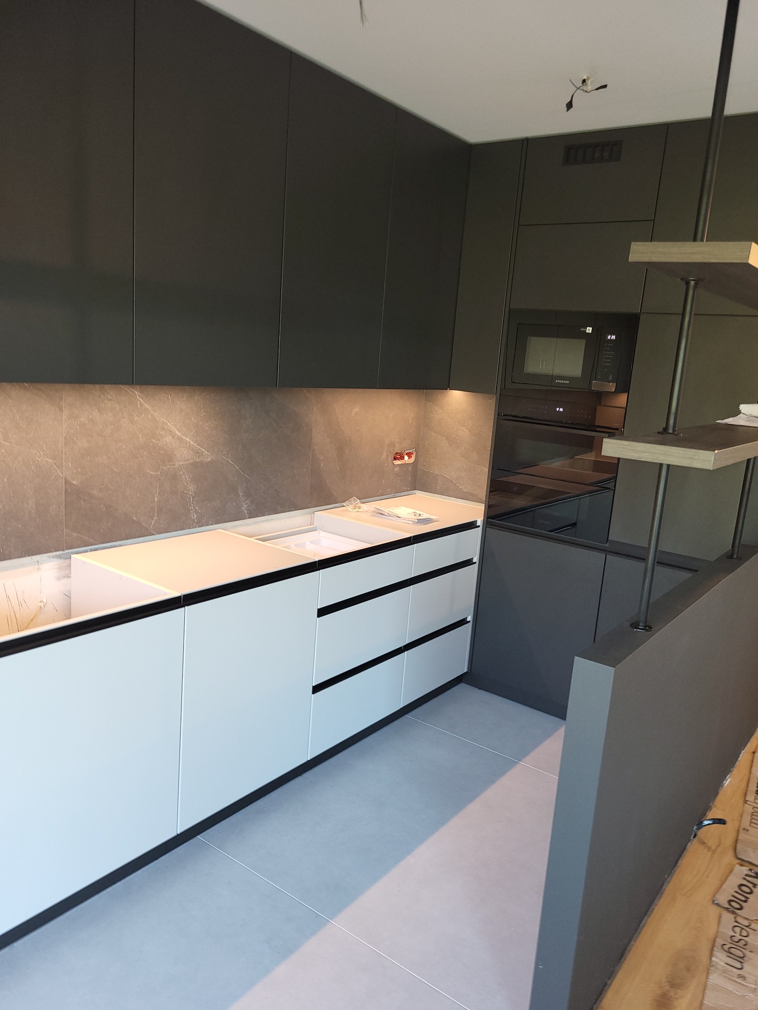 Nowoczesna kuchnia z białymi dolnymi szafkami i ciemnoszarymi górnymi, z marmurowym blatem i wbudowanym piekarnikiem, oświetlona listwą LED pod szafkami.