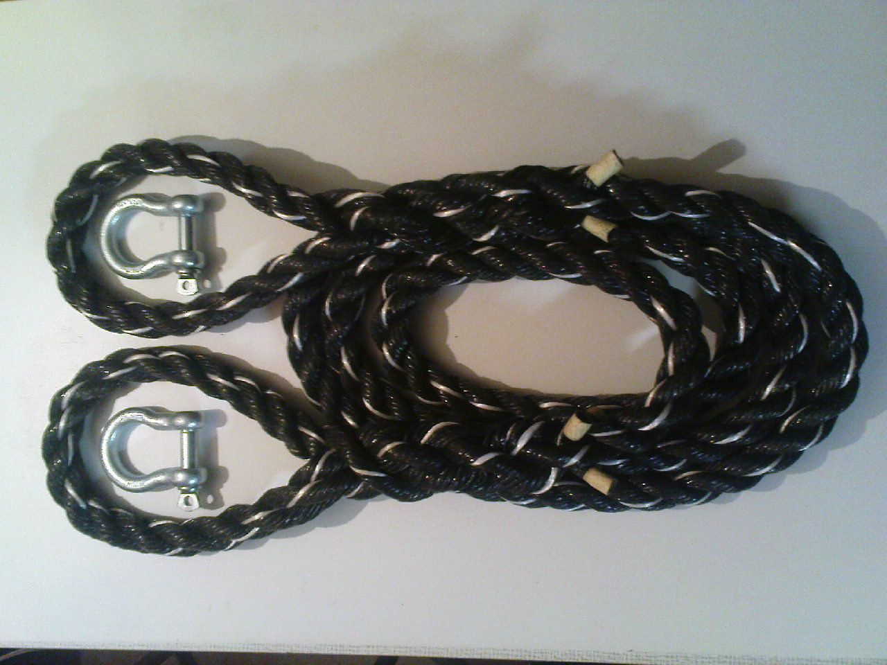 Czarna, gruba lina holownicza z dwoma metalowymi szeklami w kształcie litery U, leżąca na białym tle. Lina ma białe akcenty w splocie i jest zwinięta w owalny kształt.