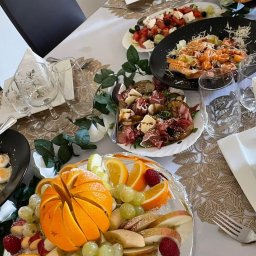 KOZACKIE JADŁO OKSANA MAKSYMENKOVA - Elegancko zastawiony stół z owocami (pomarańcze, winogrona, maliny), sałatkami i przekąskami. Dekoracja stołu z dbałością o detale, idealna na przyjęcie.