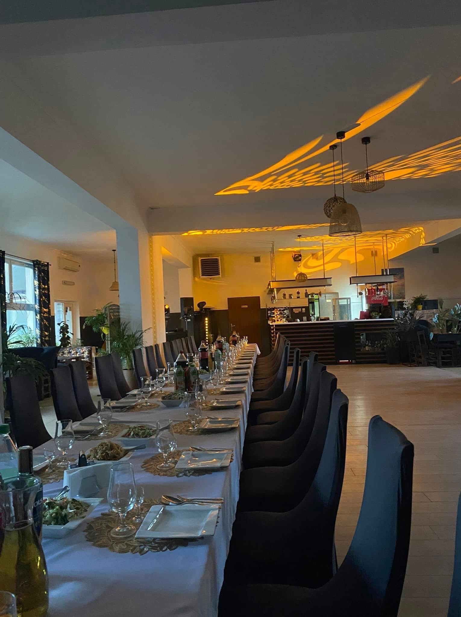 Uroczysta sala bankietowa z długim stołem nakrytym do przyjęcia, ustawionym pod dekoracyjnymi lampami rzucającymi wzory na sufit.