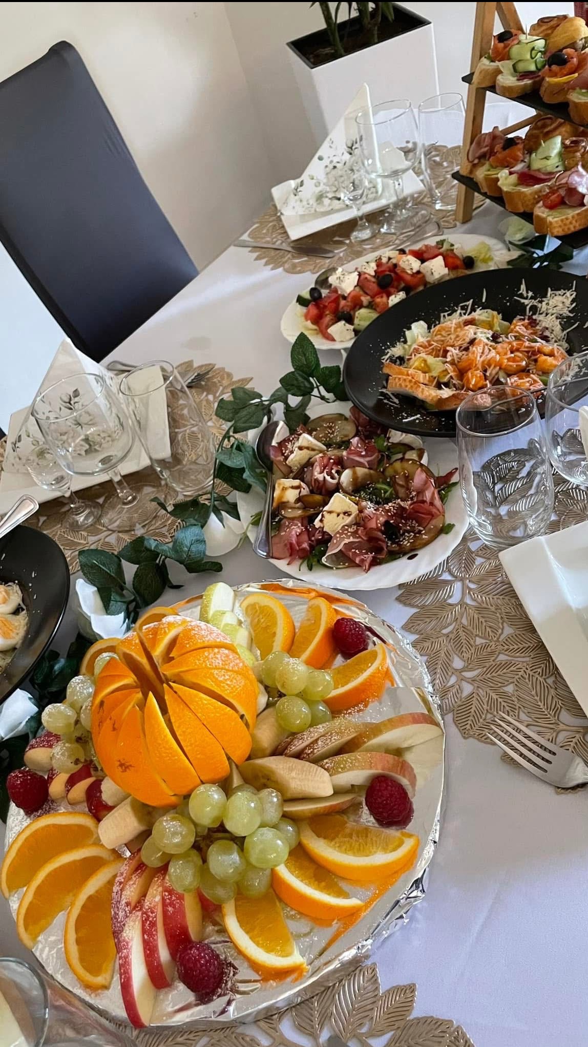 Elegancko zastawiony stół z owocami (pomarańcze, winogrona, maliny), sałatkami i przekąskami. Dekoracja stołu z dbałością o detale, idealna na przyjęcie.