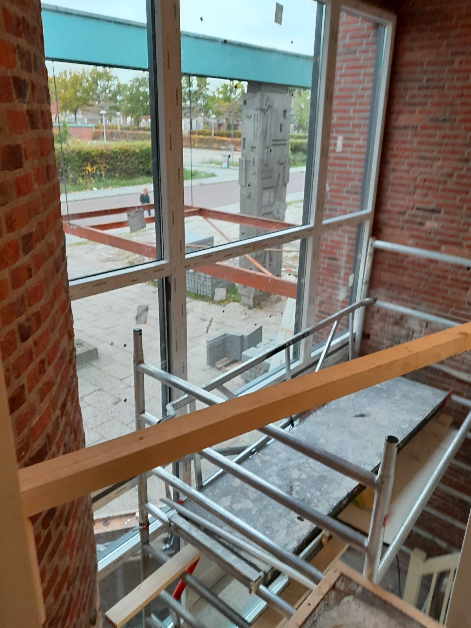 Wnętrze w trakcie prac: rusztowanie przy oknie z widokiem na zewnątrz, surowa cegła na ścianie. Etap prac wykończeniowych w pomieszczeniu.