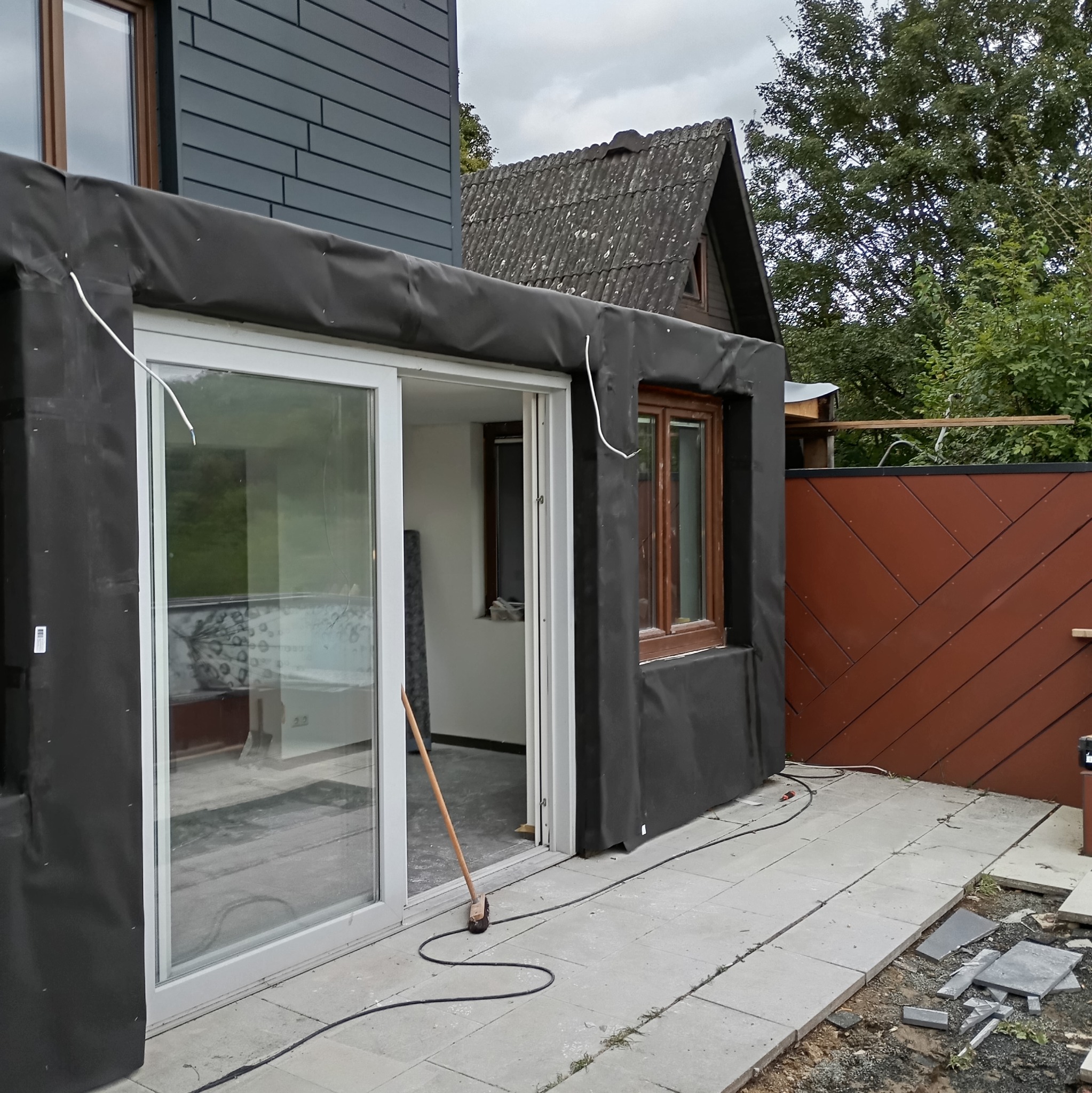 Ocieplenie budynku z oknami i przesuwnymi drzwiami, widoczne przygotowania do prac wykończeniowych, nieukończona podłoga z płyt.