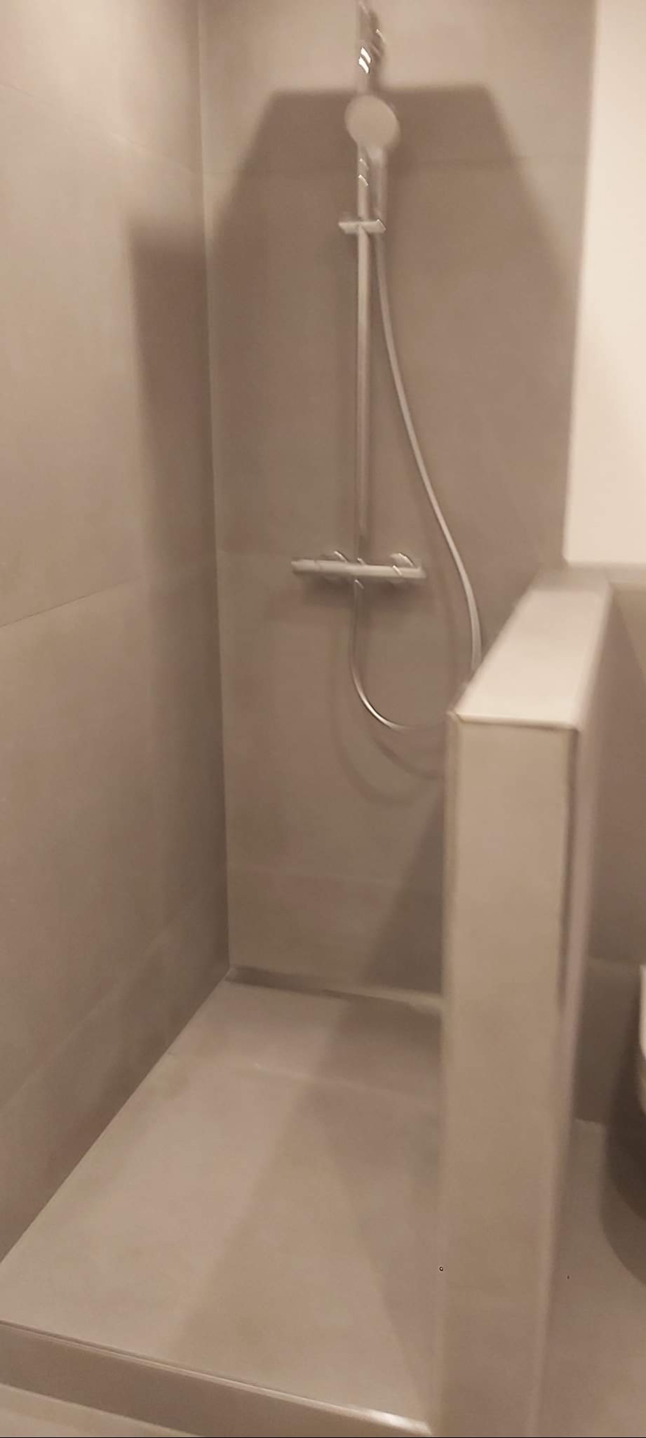 Wykończony, minimalistyczny prysznic z szarymi płytkami i chromowaną armaturą. Widoczny odpływ liniowy. Ujęcie z dołu, podkreślające prostotę i nowoczesność.