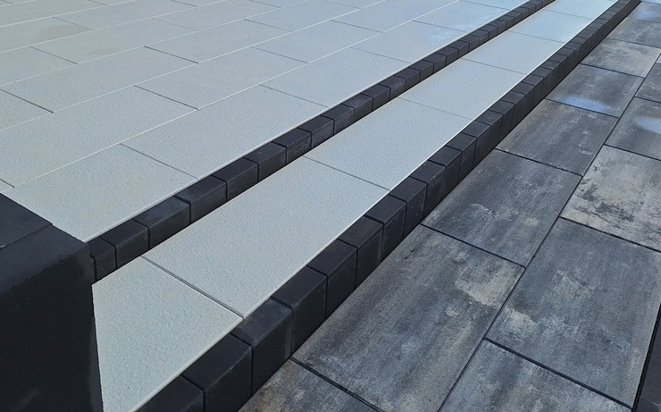 Schody z kostki brukowej: jasnoszare płyty prostokątne obramowane ciemnoszarą kostką, przechodzące w szare płyty. Nowoczesny design.