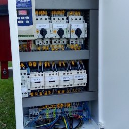 energon - Otwarta szafa sterownicza z kontrolerem Bonfiglioli Vectron, rzędami opisanych styczników do sterowania ruchem (góra, dół, przód, tył) i okablowaniem. Na dole leży etykieciarka Dymo.