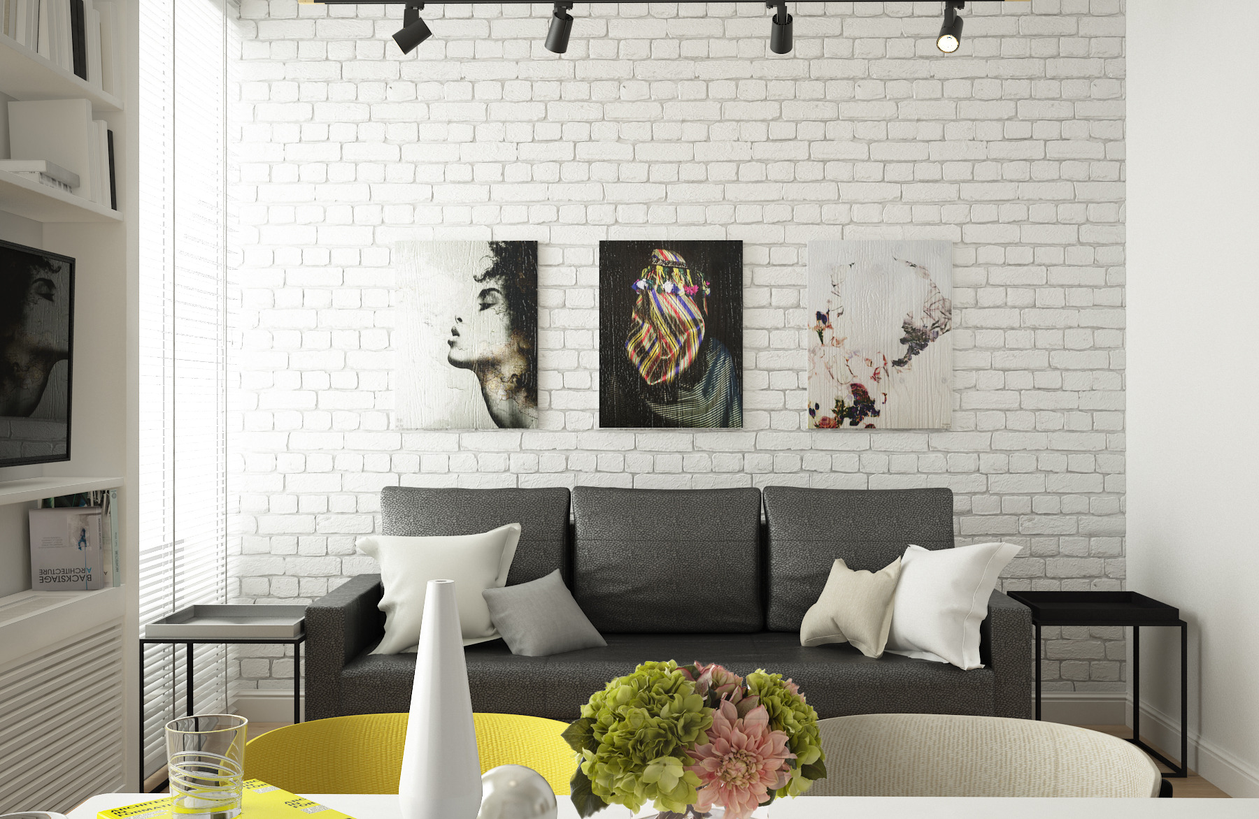 Salon z szarą sofą, białymi poduszkami i trzema obrazami na białej ceglanej ścianie. Na stole wazon z kwiatami. Nowoczesne oświetlenie sufitowe.