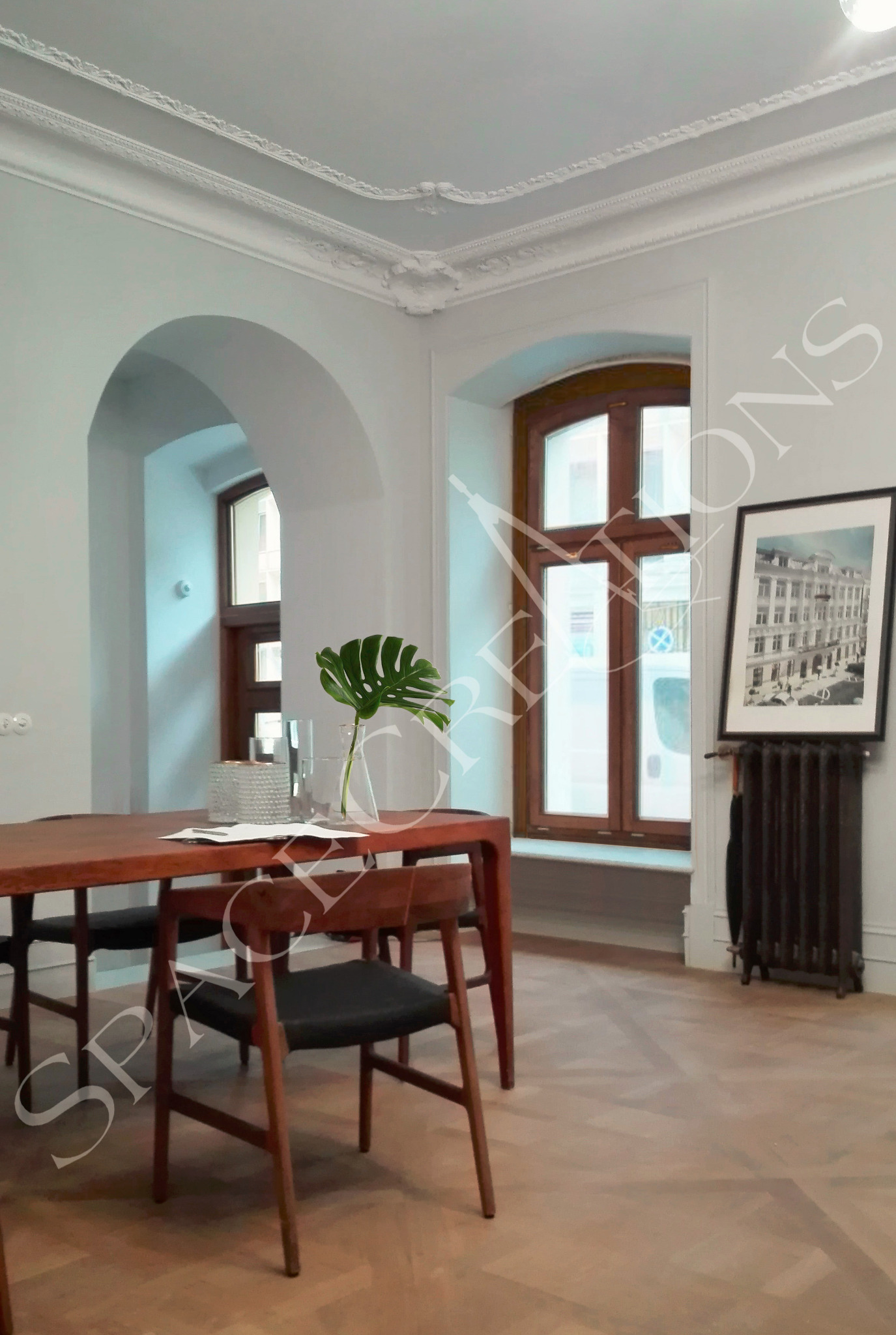 Stylowa jadalnia w Warszawie: drewniany stół z krzesłami, parkiet w jodełkę, dekoracyjny sufit, okno z drewnianą ramą i obraz w czarnej ramie.