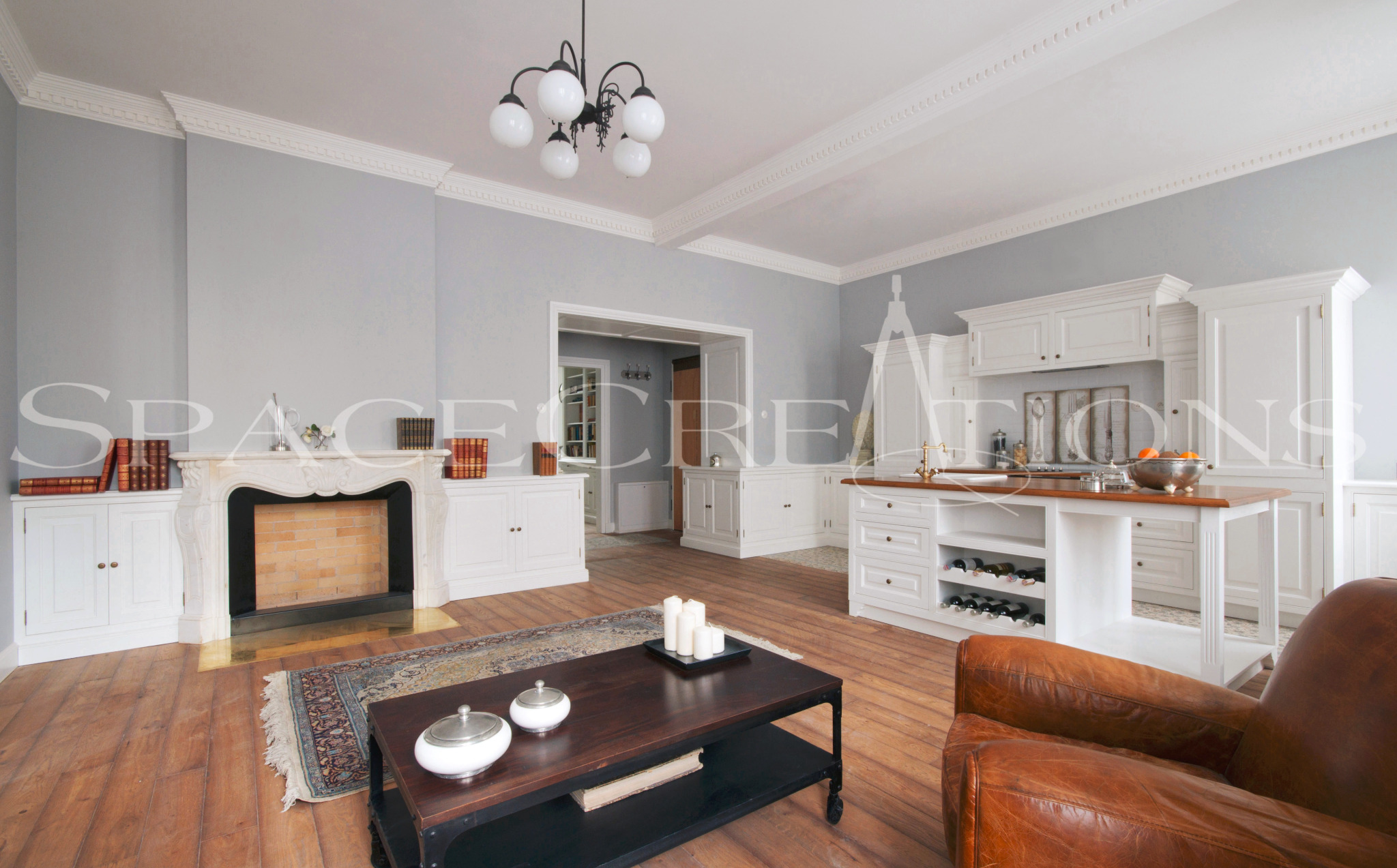 Eleganckie wnętrze z marmurowym kominkiem, drewnianą podłogą, białą zabudową kuchenną i wyspą. W tle widoczne przejście do kolejnego pomieszczenia.