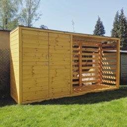 Produkcja więźby dachowej, opakowań i galanterii drzewnej Janusz Łukasiewicz - Nowoczesna drewutnia z drewna, zamykana na klucz, z ażurową częścią na drewno, na tle zielonej trawy i drzew. Funkcjonalny domek narzędziowy.