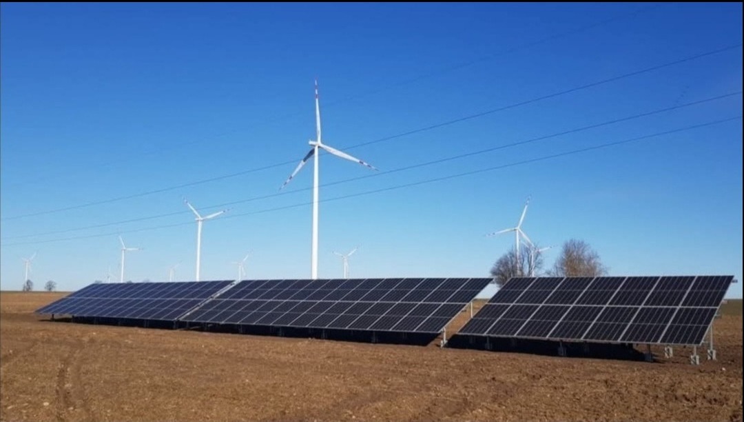 Instalacja paneli fotowoltaicznych w Działdowie na polu, z turbinami wiatrowymi w tle i błękitnym niebem.