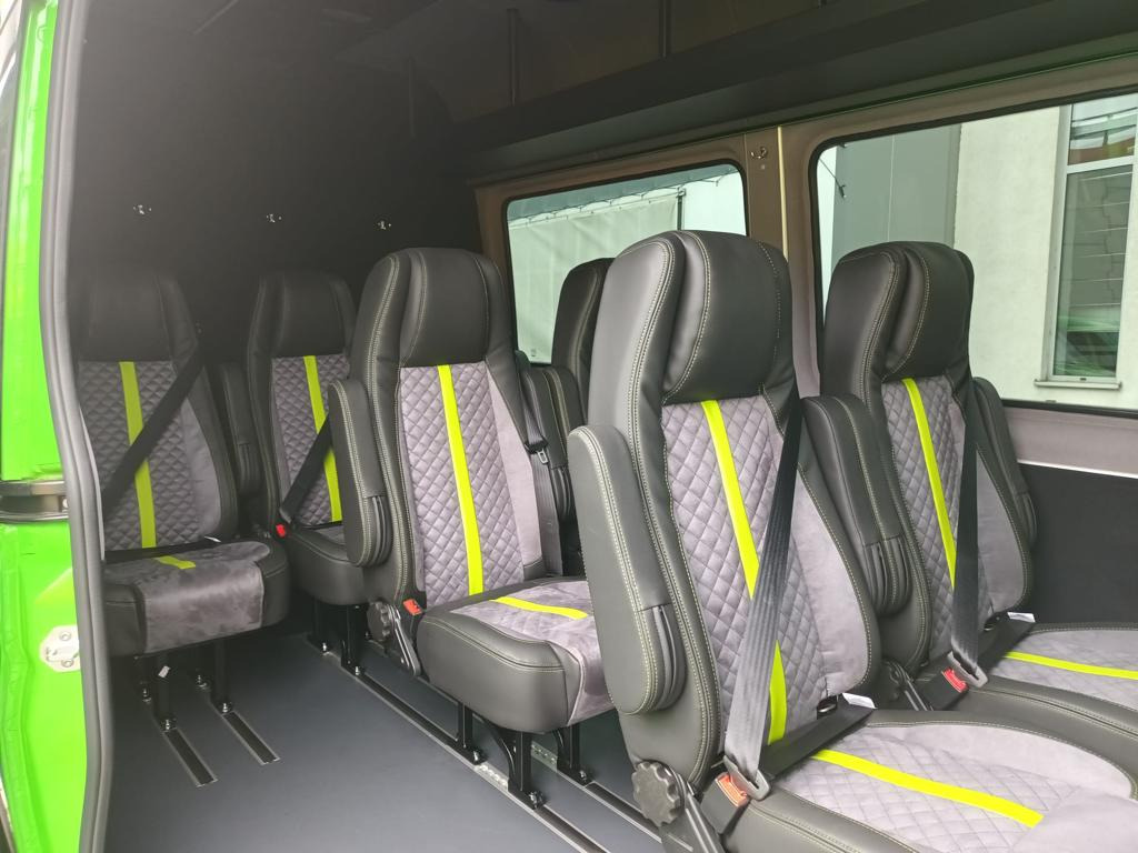 Wnętrze busa z luksusowymi, szarymi fotelami z pikowaniem i neonowo-żółtymi pasami. Fotele z podłokietnikami, regulowane, z pasami bezpieczeństwa. Widok na okno.
